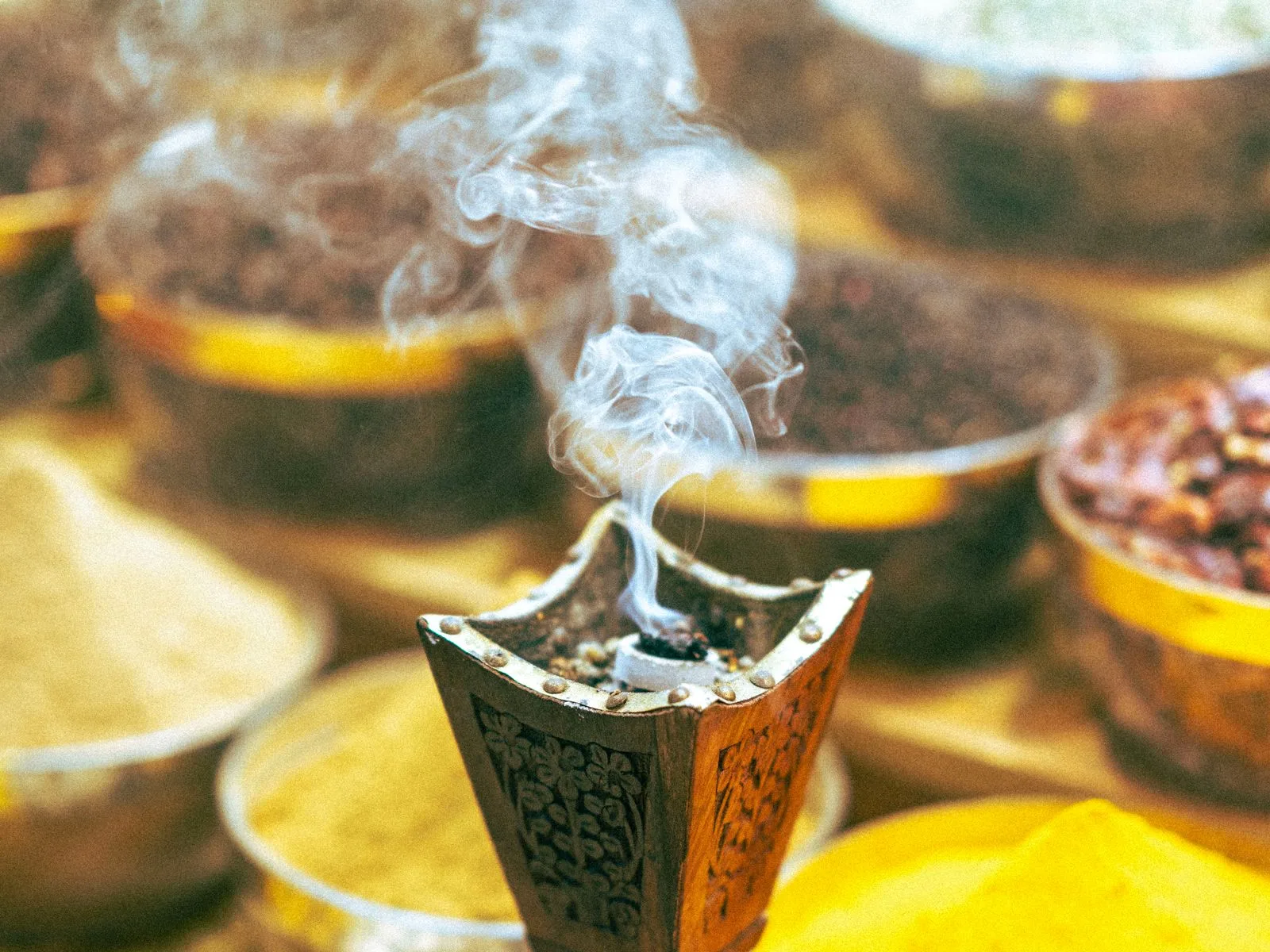 Traditional Arabic incense burner with oud smoke, surrounded by bowls of bakhoor and spices